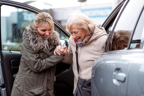 an adult woman helping an elderly woman out of a car