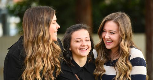 Three teenage young women smiling and laughing together.