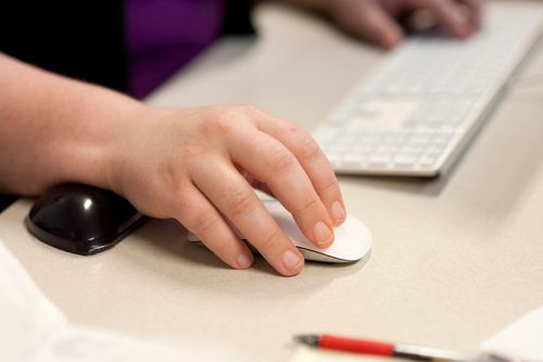 A woman’s hand is pictured using a computer mouse, with her other hand resting on a keyboard.