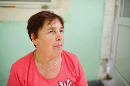 A woman with short dark hair and a pink T-shirt sits near a green wall in Romania.