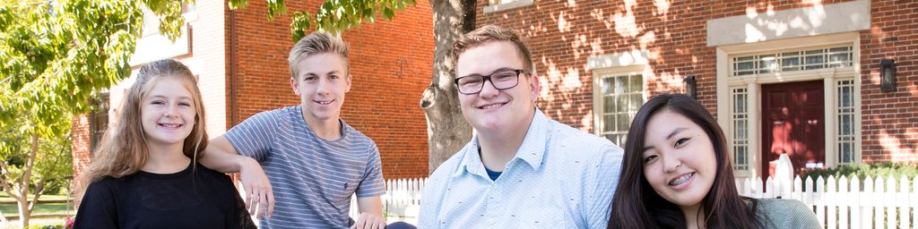 Group of four youth smiling while in front of two red brick buildings.