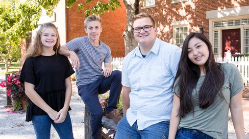 Group of four youth smiling while in front of two red brick buildings.