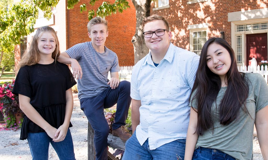 Group of four youth smiling while in front of two red brick buildings.