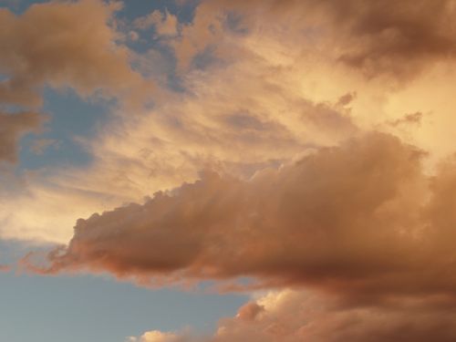 Clouds lie low during a sunset and turn orange under a blue sky.
