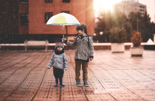 Garotinho segurando o guarda-chuva para uma criança