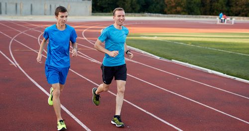 Two young men are outside. They are running on a track. This is in Lisbon, Portugal.