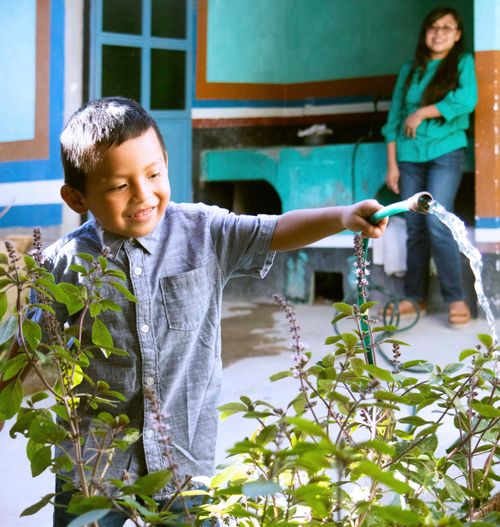 A little boy watering plants with a hose