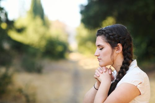A young adult woman praying in wooded area.