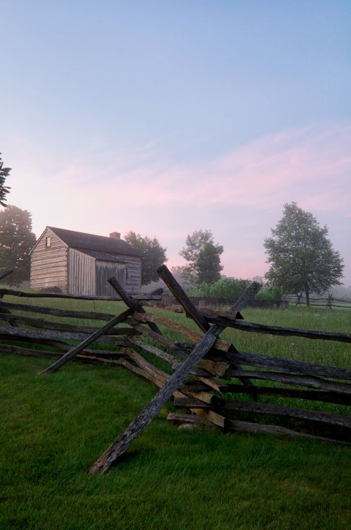 A wooden fence in the foreground and an old log cabin in the background on the Smith family farm in Palmyra, New York.