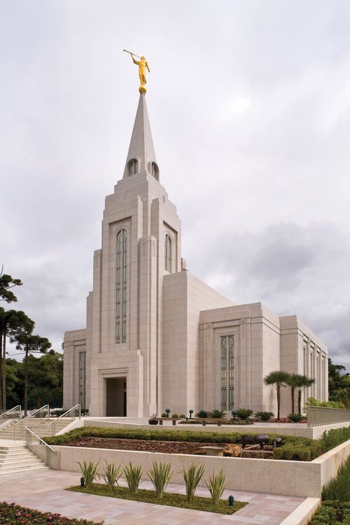 The Curitiba Brazil Temple on an overcast day, with large flower beds lined with green plants in the front.