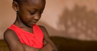 A young African girl with her head bowed and arms folded in prayer.  Taken in Ghana, West Africa.