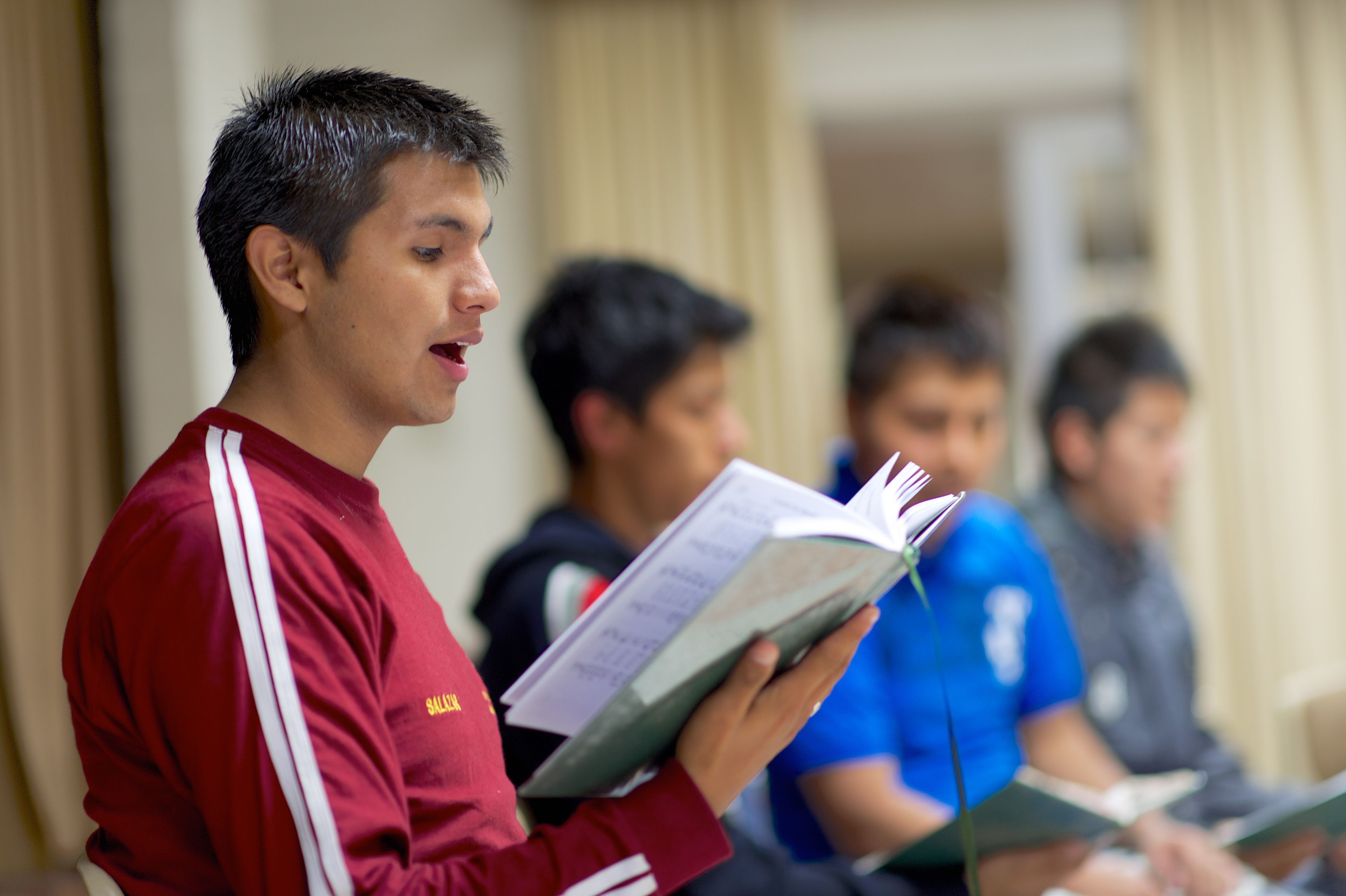 A group of young men in Peru sing from a hymnbook during a Mutual activity.