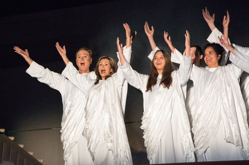 Adult male and female angels wearing white and singing with raised arms in the Arizona Christmas pageant.
