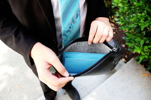 A young man holds open a fast-offering pouch to show a few blue fast-offering envelopes.