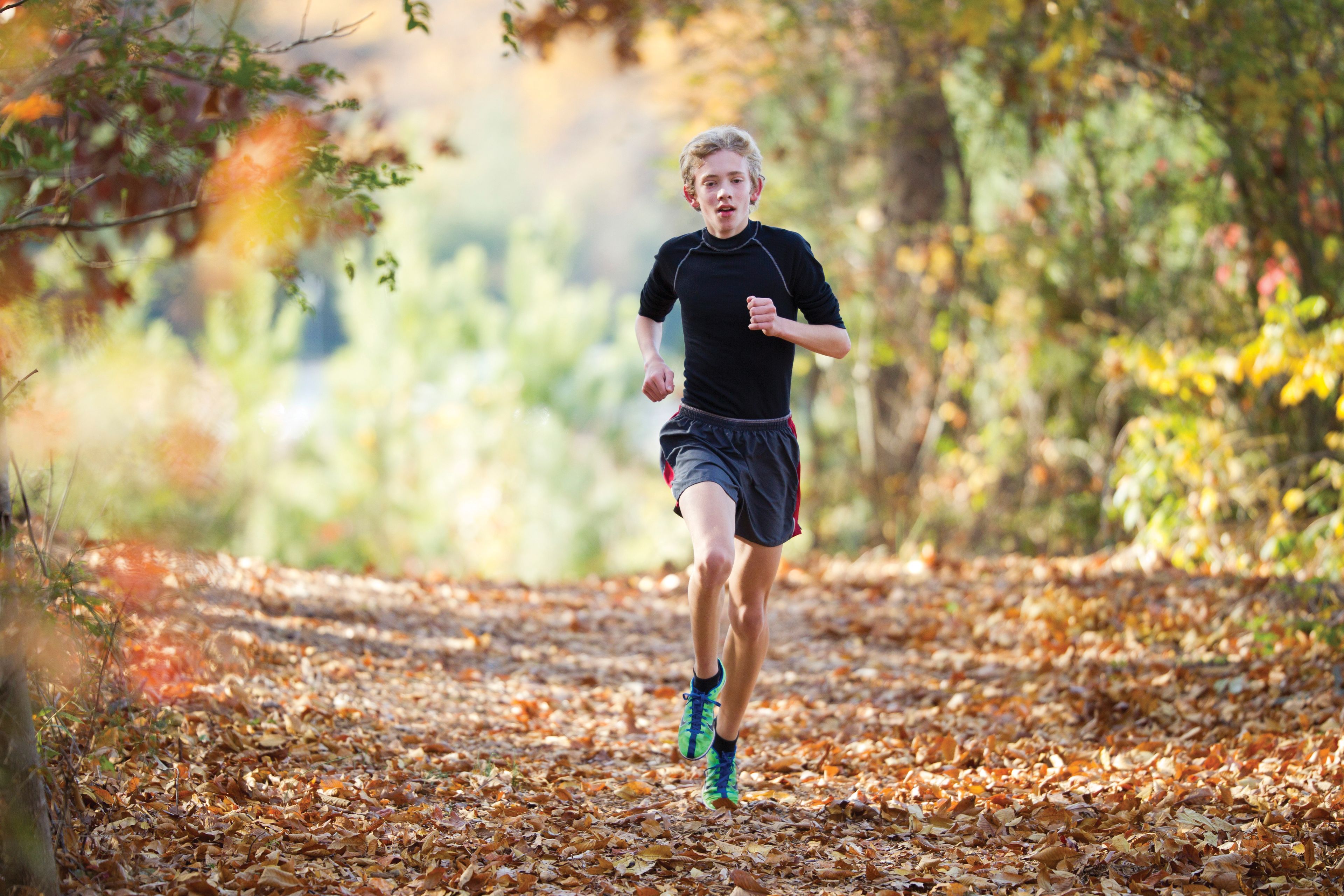 A young man running outside down a path with leaves.