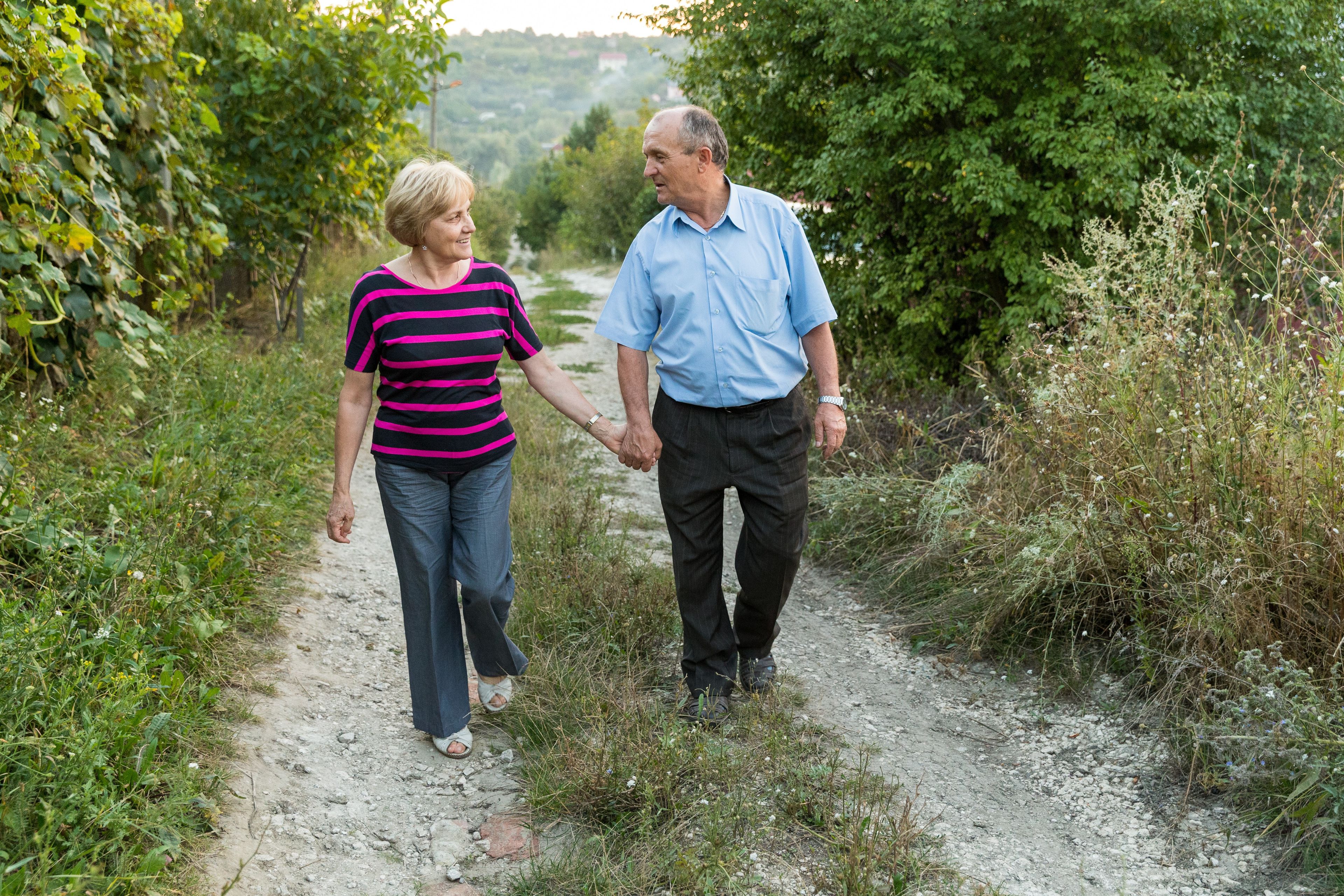 An elderly couple from Moldova holding hands and walking on a road together.