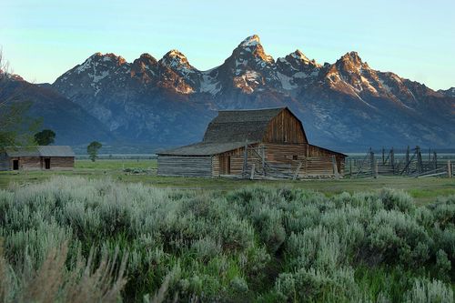 An old wooden barn with the Teton Mountains in the background.