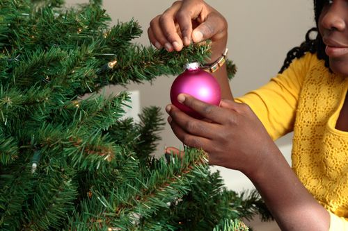 A Ghanaian girl decorates a Christmas tree with a glossy pink ornament.
