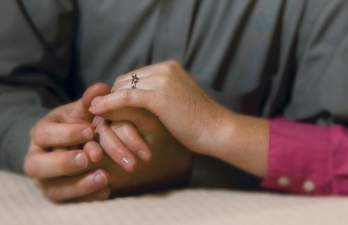 Close-up of the hands of a couple kneeling by a bed praying together.