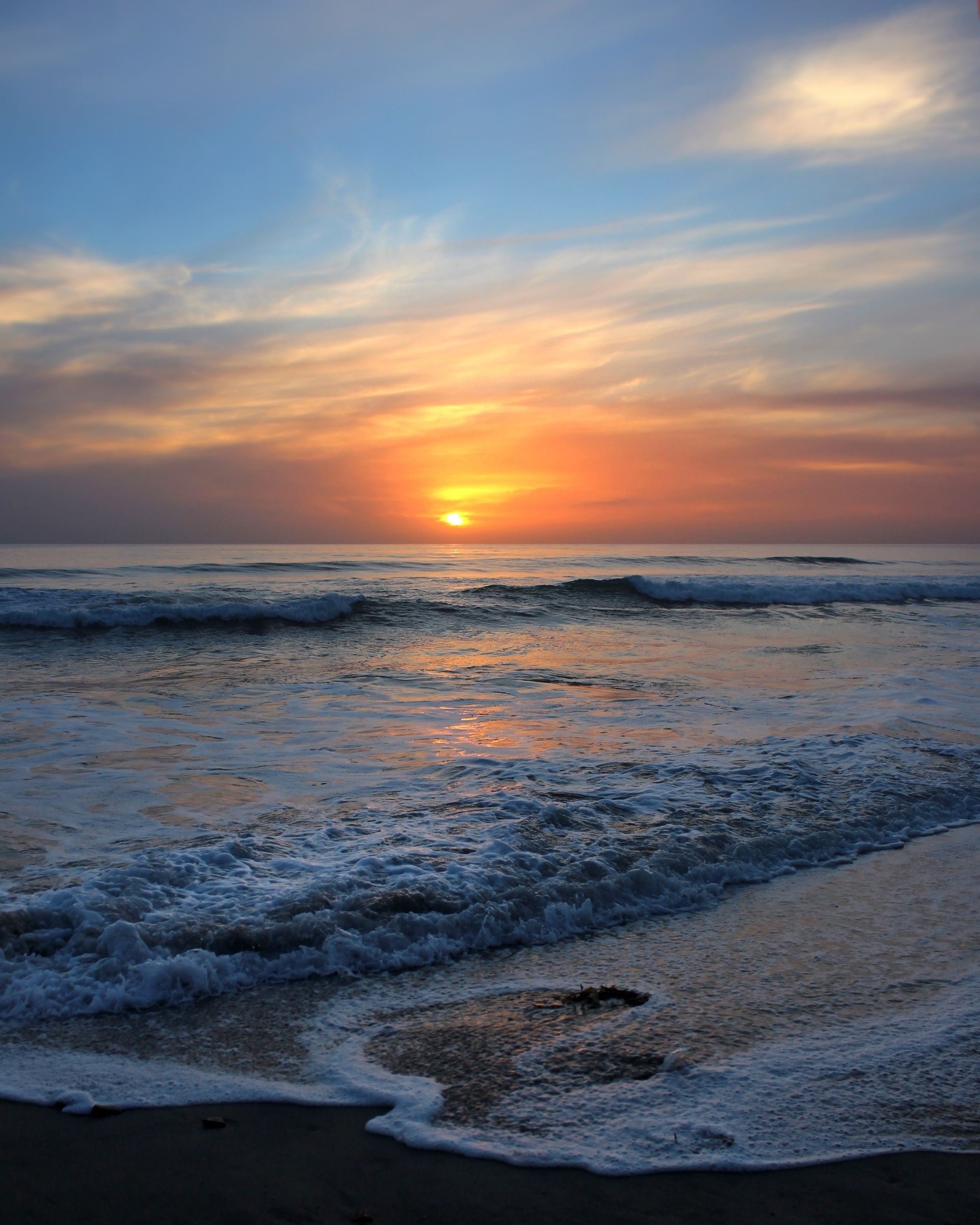 The sun sets over waves crashing on a beach.