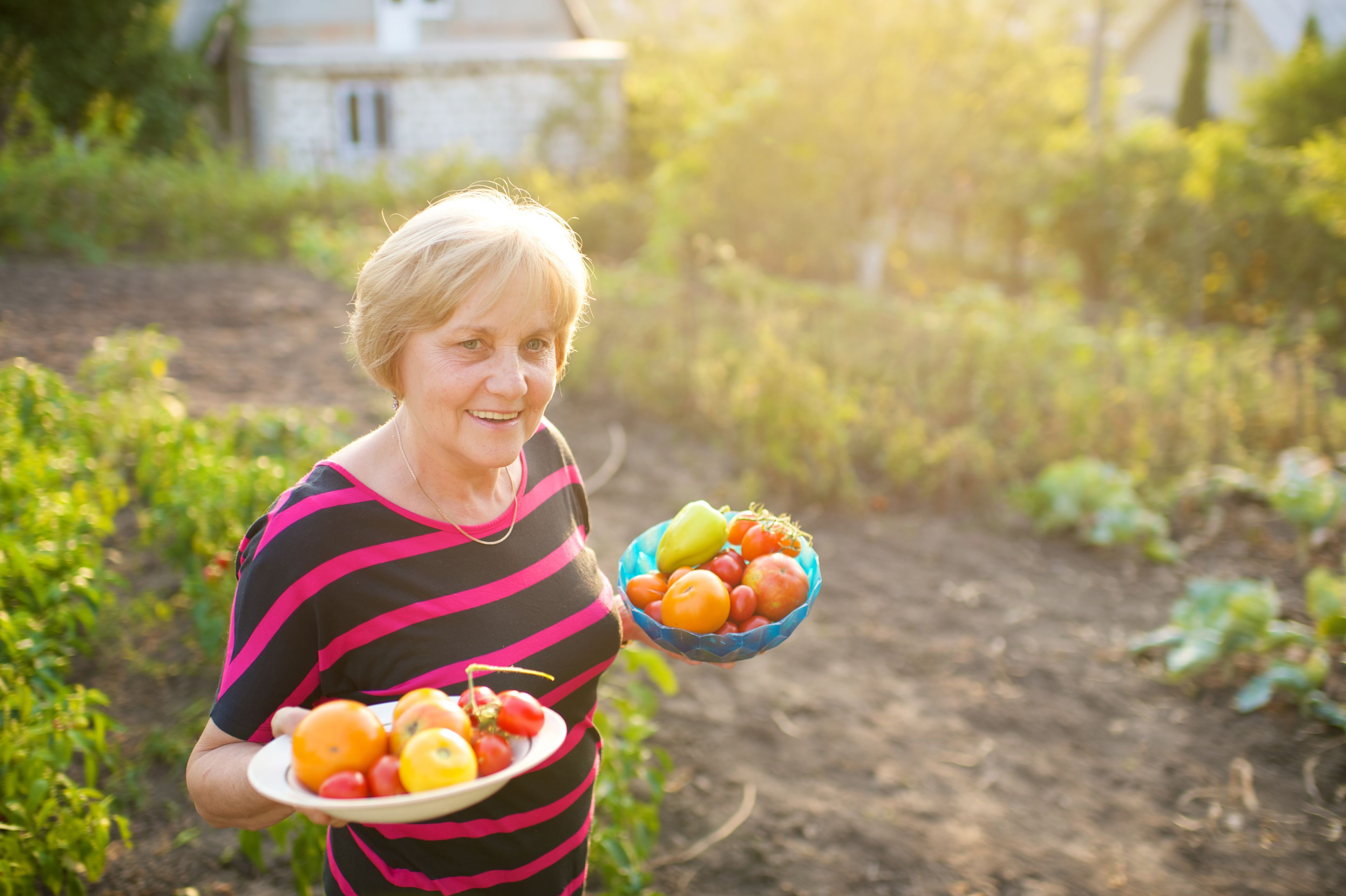 A woman in Romania holds two bowls full of fresh vegetables from the garden.
