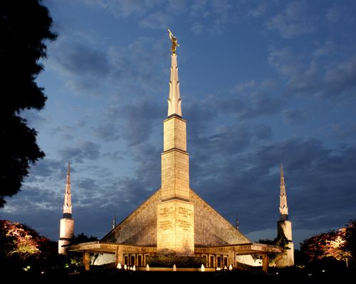 The front spires of the Dallas Texas Temple lit up at night, with a deep blue sky in the background.