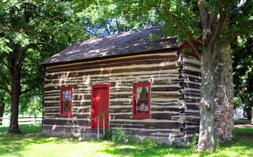 A log cabin with a red door and red-framed windows, surrounded by trees in Fayette, New York.