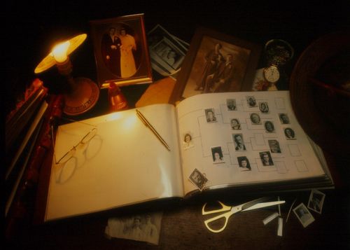 A pedigree chart in a book of remembrance with family pictures and other objects lying nearby.