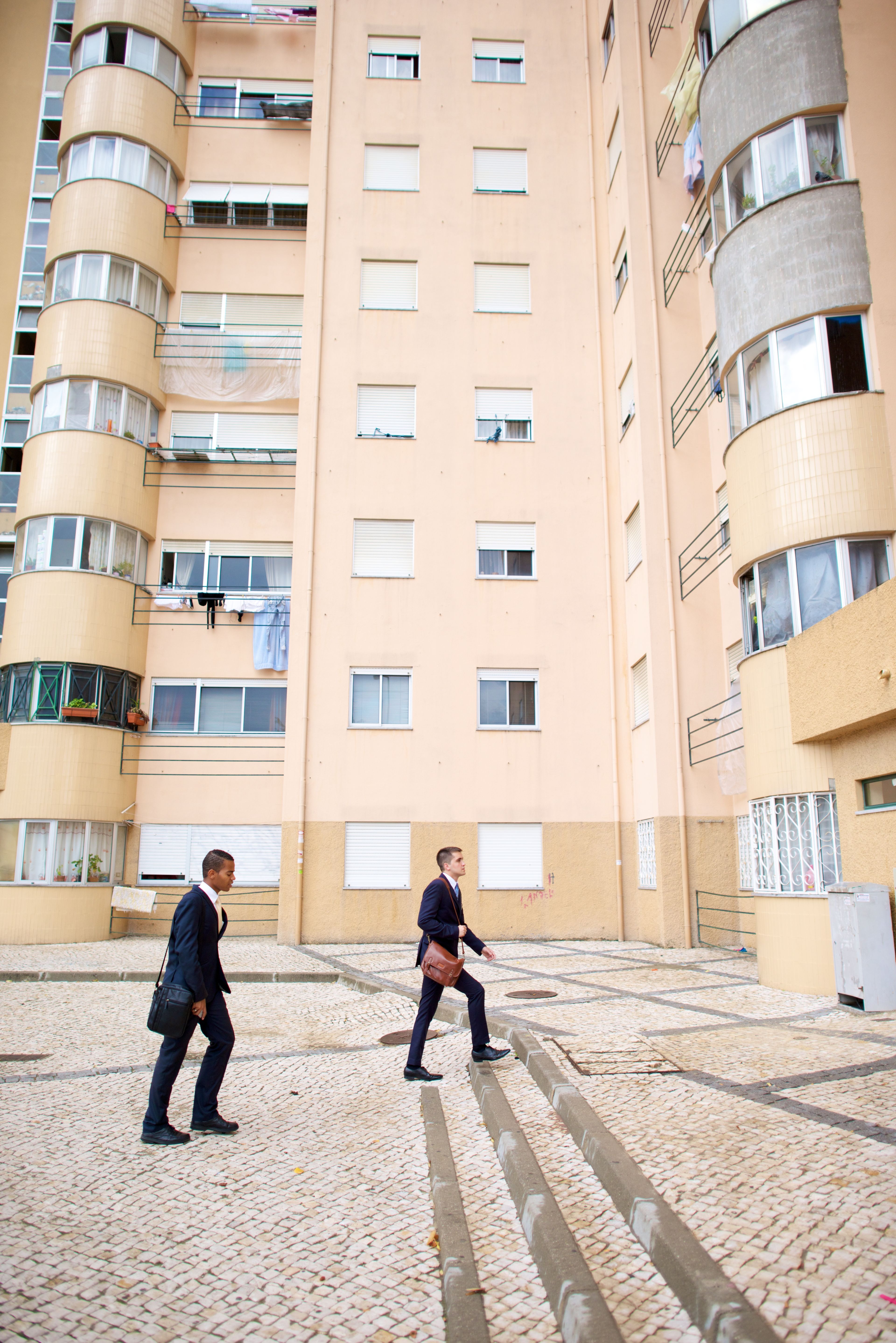 Two elder missionaries walking beside tall buildings in Portugal.
