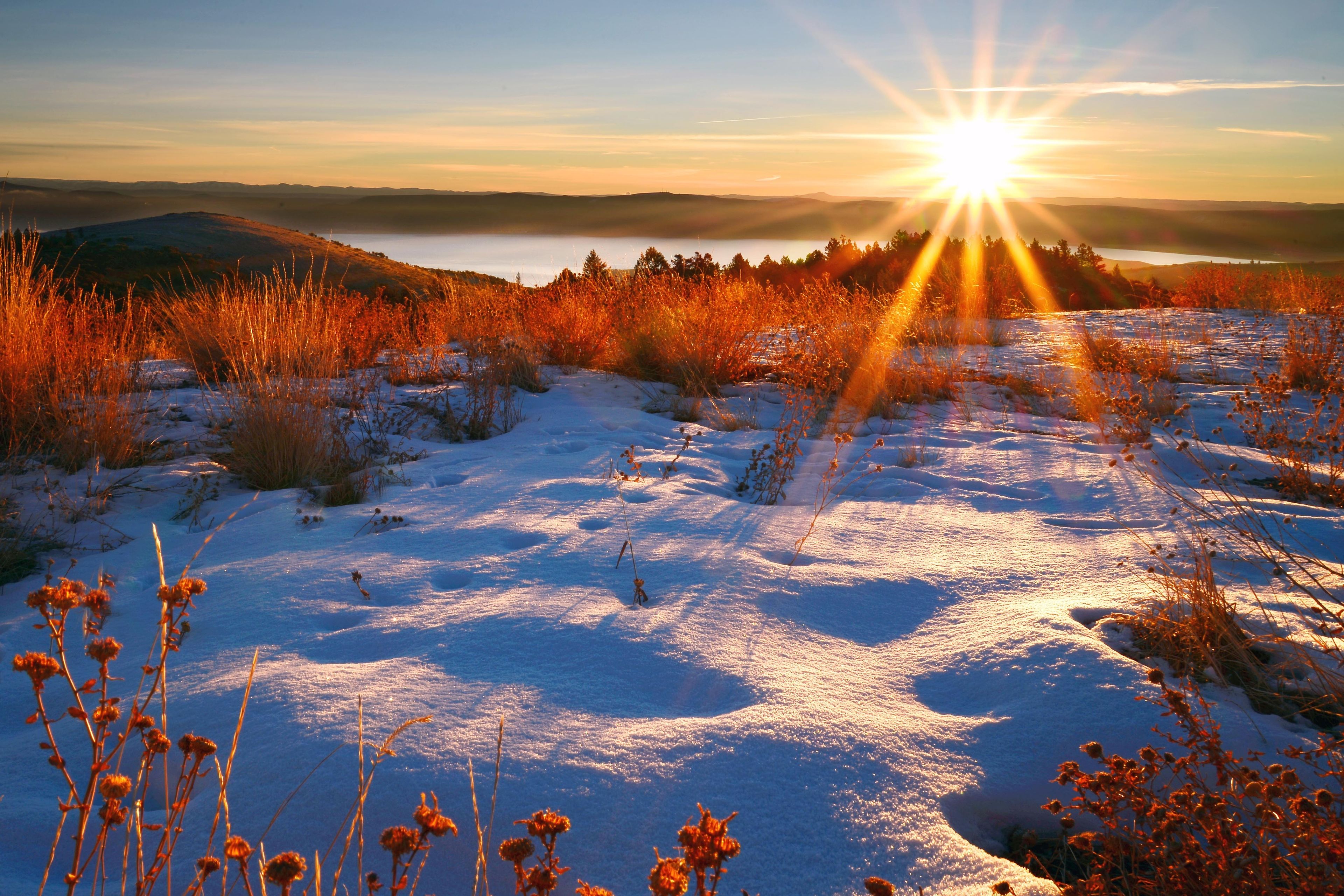The sun rises over a lake surrounded by snow.