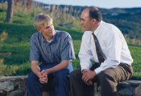 A father sitting on a stone fence with his teenage son. The father and son are looking at each other as they counsel together. Posed by models.