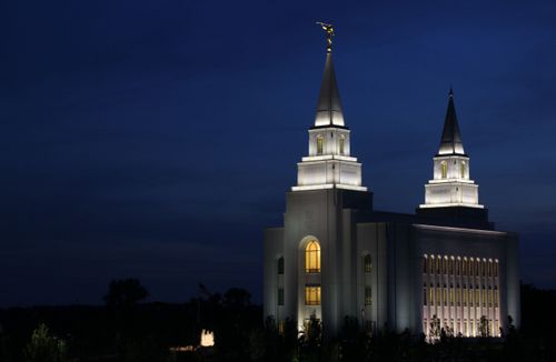 A front view of the Kansas City Missouri Temple at night, illuminated by the lights outside and inside the temple, with a dark sky in the background.