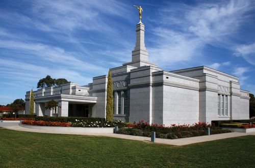The exterior of the Adelaide Australia Temple in the daytime, with a green lawn and flowers in the flower beds.