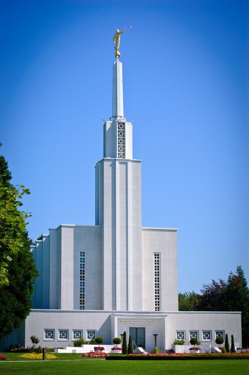 The front of the Bern Switzerland Temple on a sunny day, with green lawns and trees and blooming flowers in the flower beds.