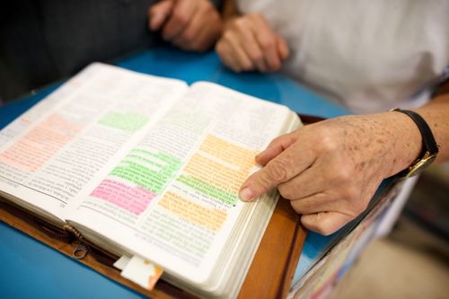 A woman pointing at a green-highlighted verse in a well-marked set of scriptures.