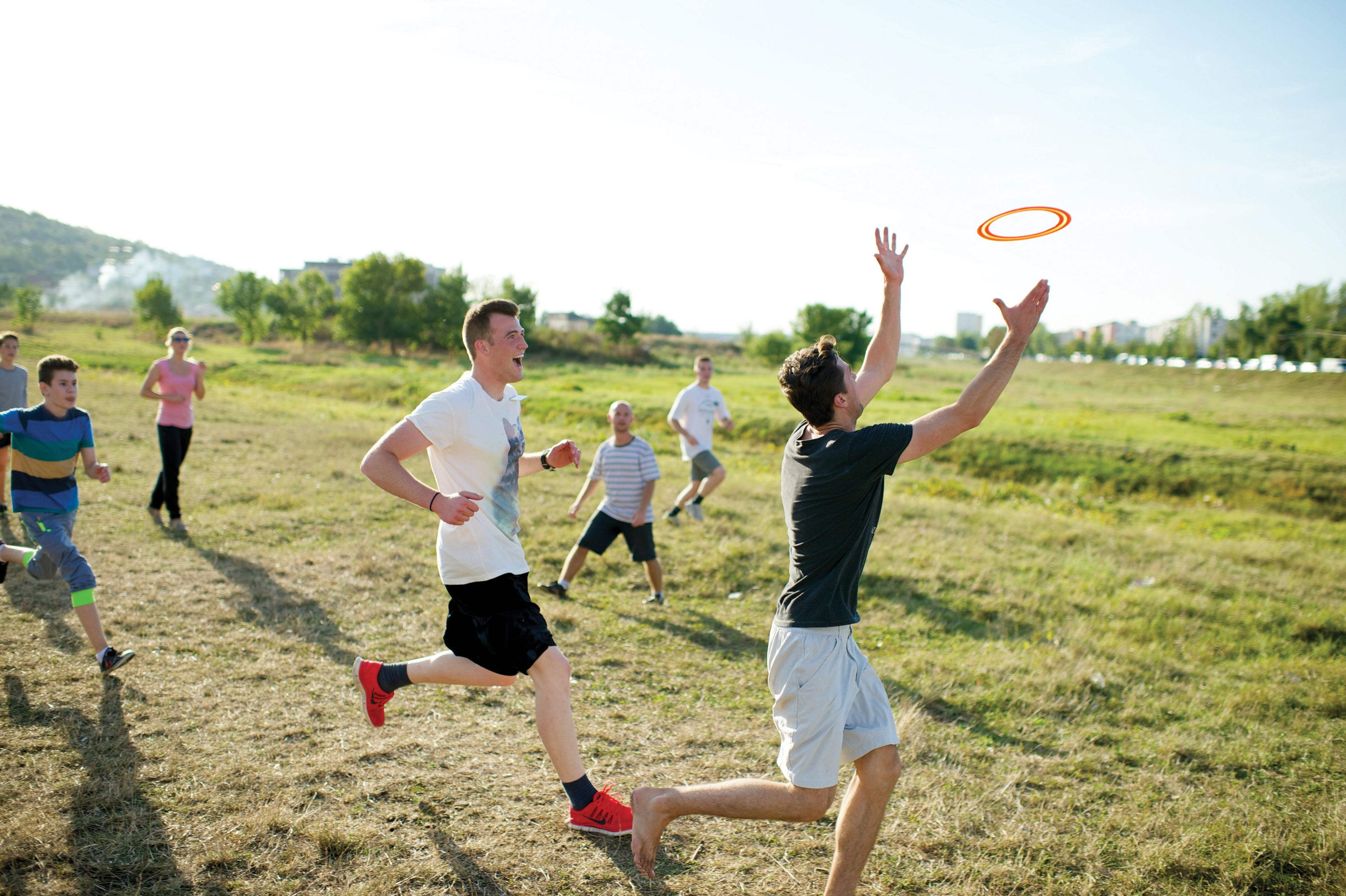 A young man reaches for a Frisbee in the air with other youth running behind him.