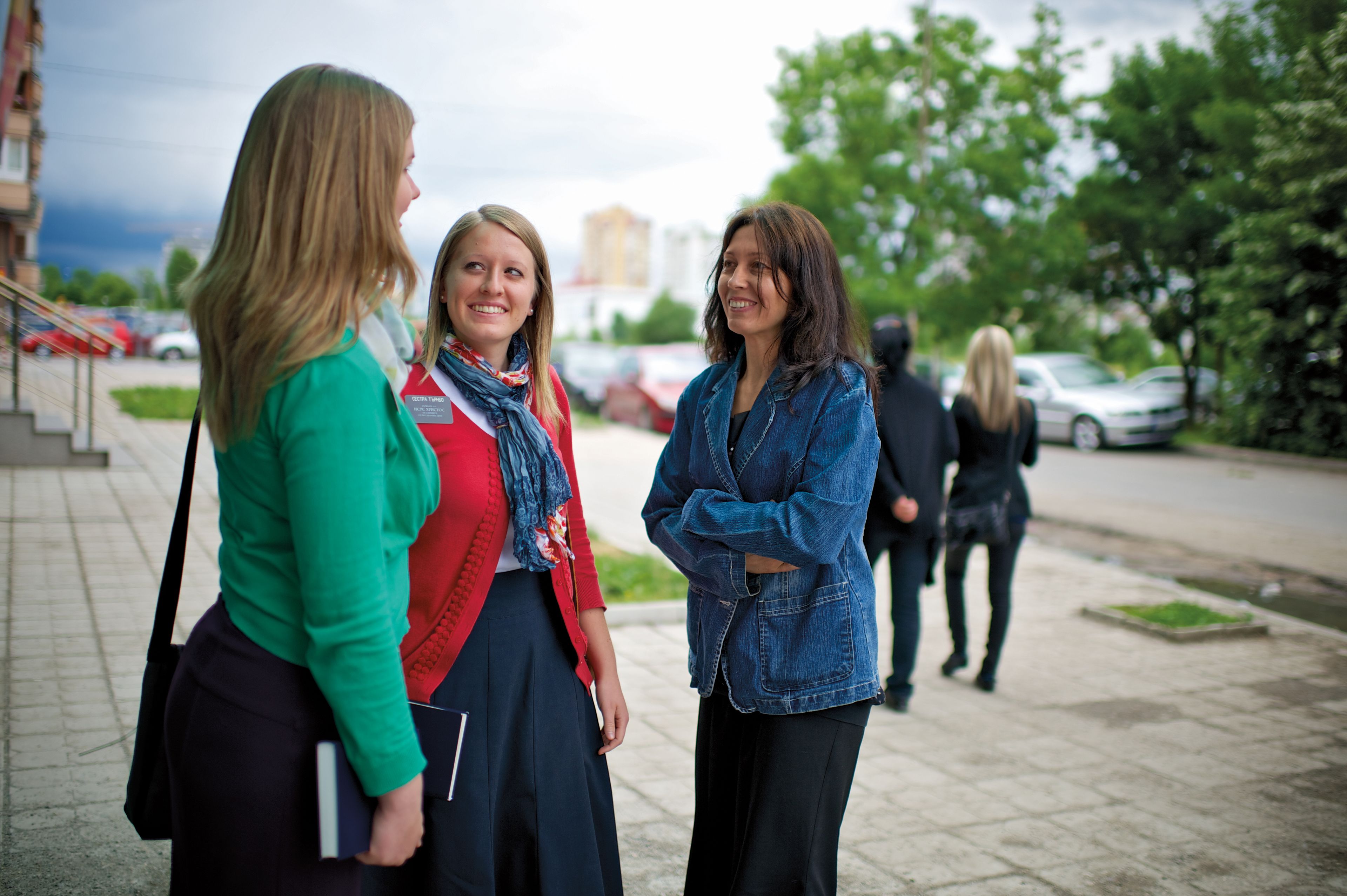 A woman talking to two sister missionaries on a sidewalk.