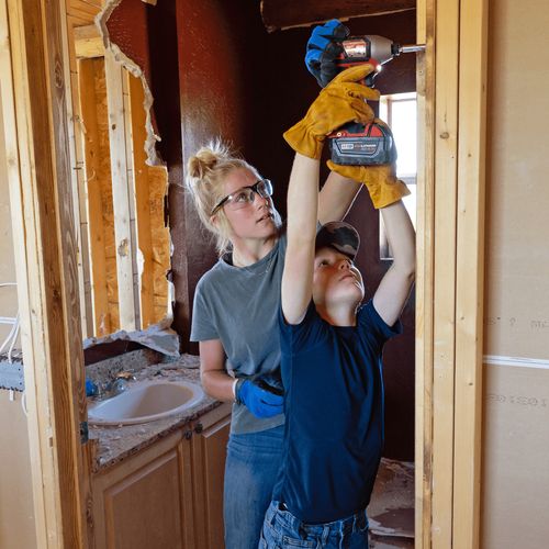 young woman helping a boy drill at a construction site