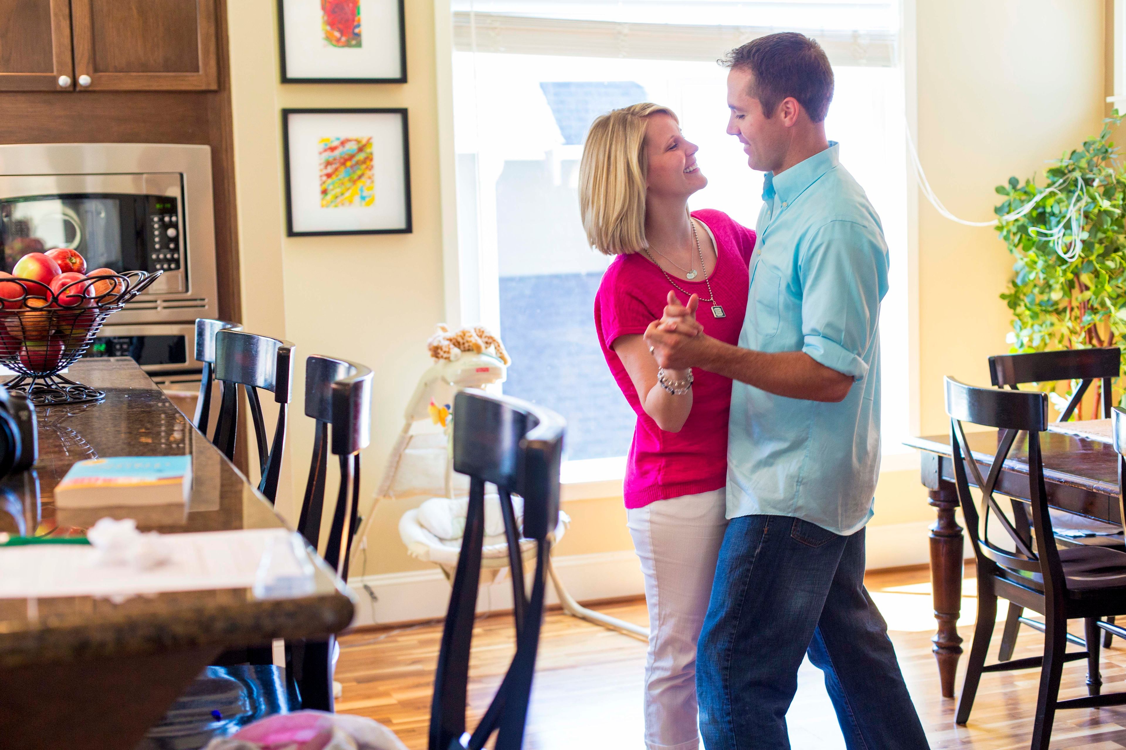 A young couple dancing in their kitchen at their home.  