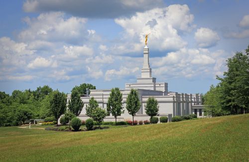 The Palmyra New York Temple seen from afar, surrounded by leafy green trees and a green lawn.