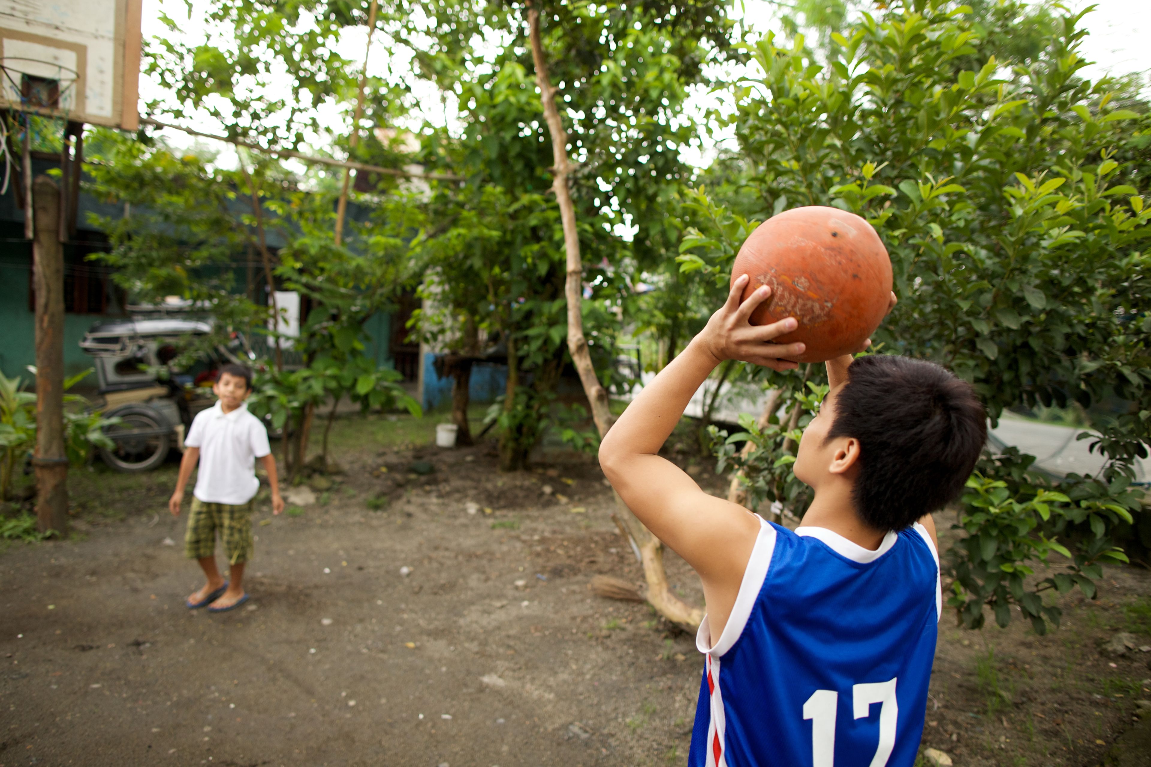 Two brothers play basketball outside on a dirt court in the Philippines.  