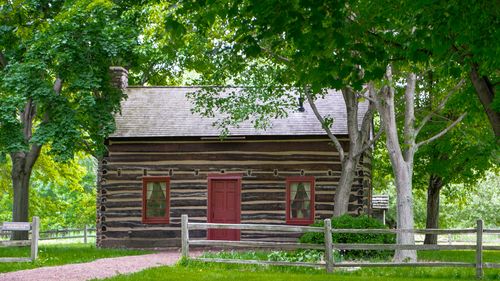 Log home surrounded by lush green trees and a low, split-rail fence.