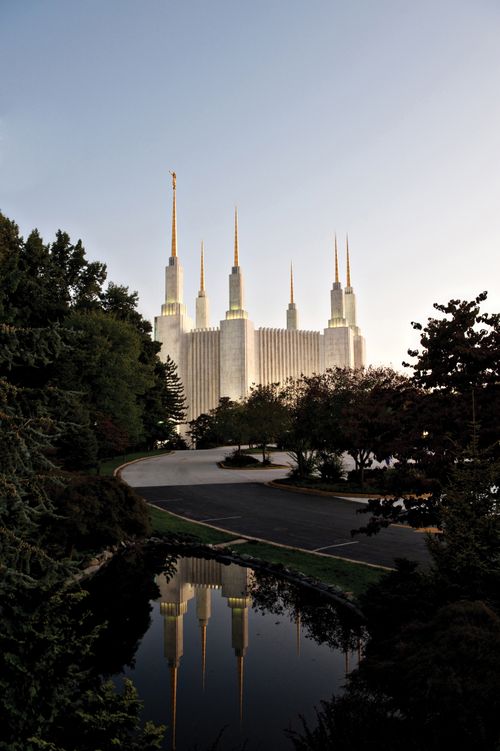 The entire Washington D.C. Temple lit up in the evening, with the reflecting pond in the foreground.