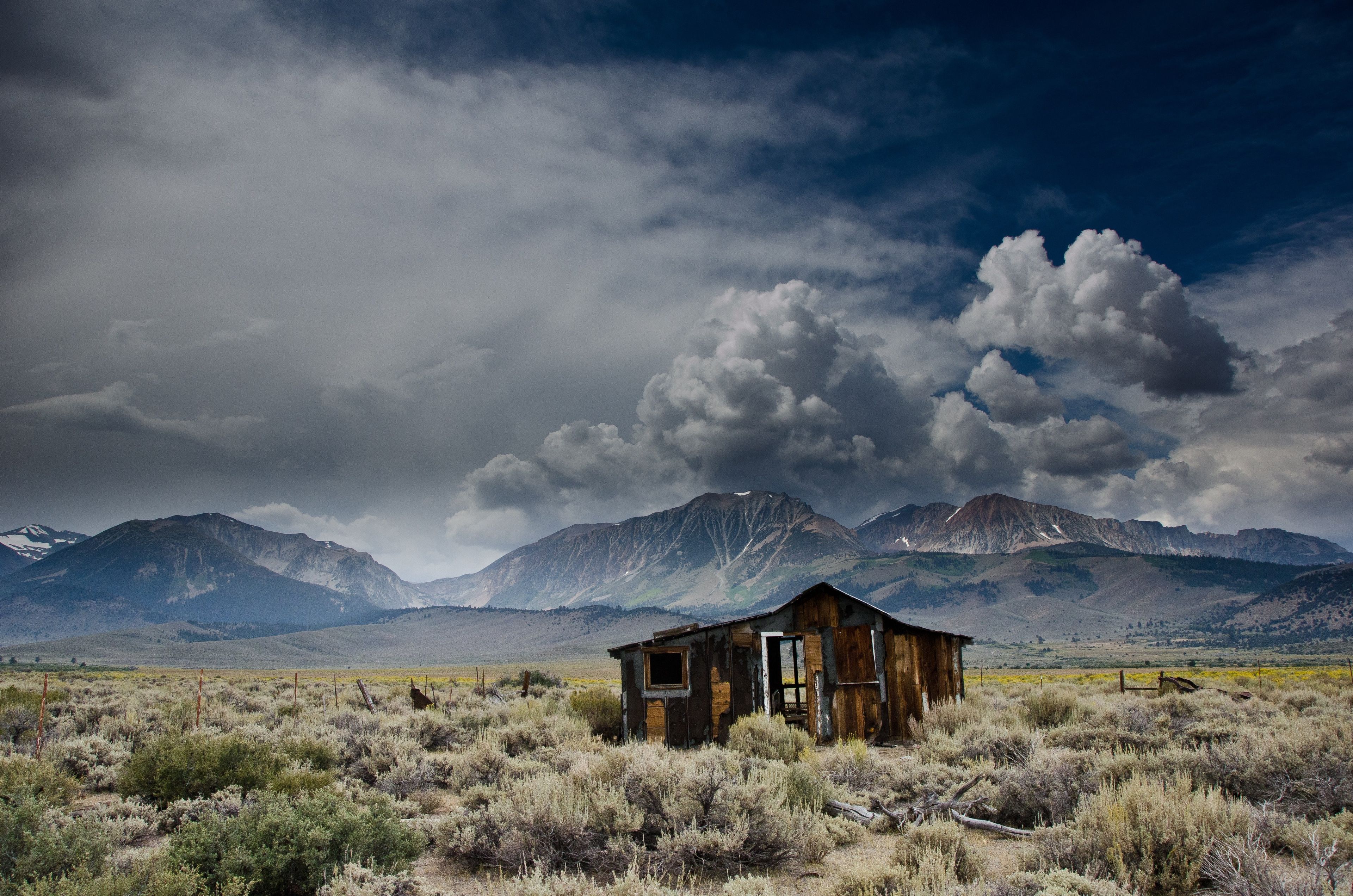 A run-down cabin in a field, with a mountain range in the background.