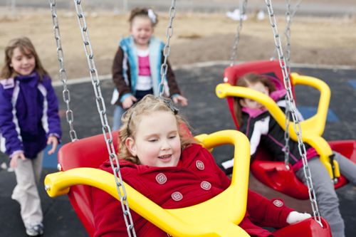 Two girls in coats push two other girls on red and yellow swings.