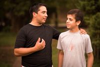 A man talking to a teenage boy in an outdoor setting.  Shot in Argentina.