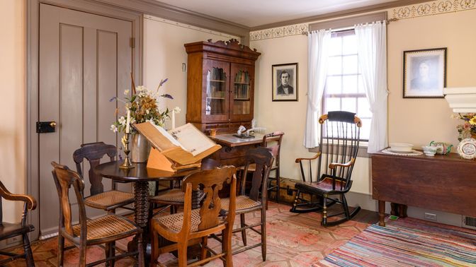 Well-lit room with a table surrounded by four chairs, a rocking chair, and other furnishings.