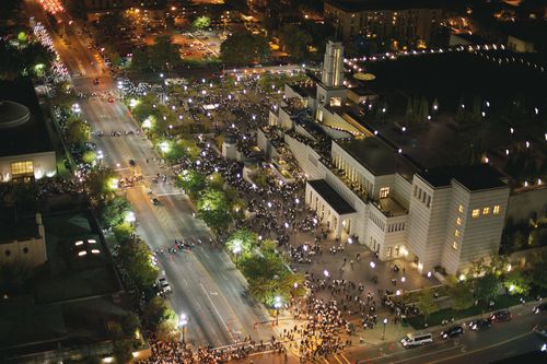 A night aerial view of the Conference Center with bright lights and with large groups of people gathered outside the building.