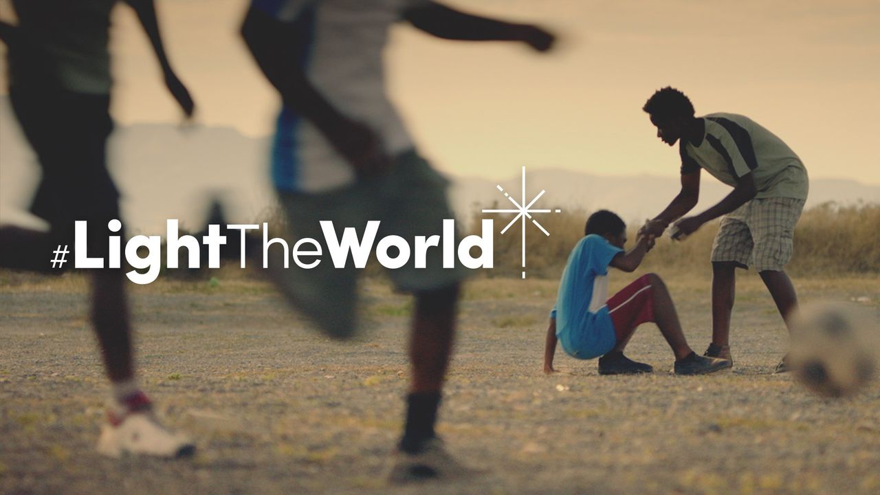Ein Junge hilft einem anderen Jungen hoch, nachdem dieser beim Fußballspielen hingefallen ist, Szene aus dem Video <i>Der Welt ein Licht<i>
