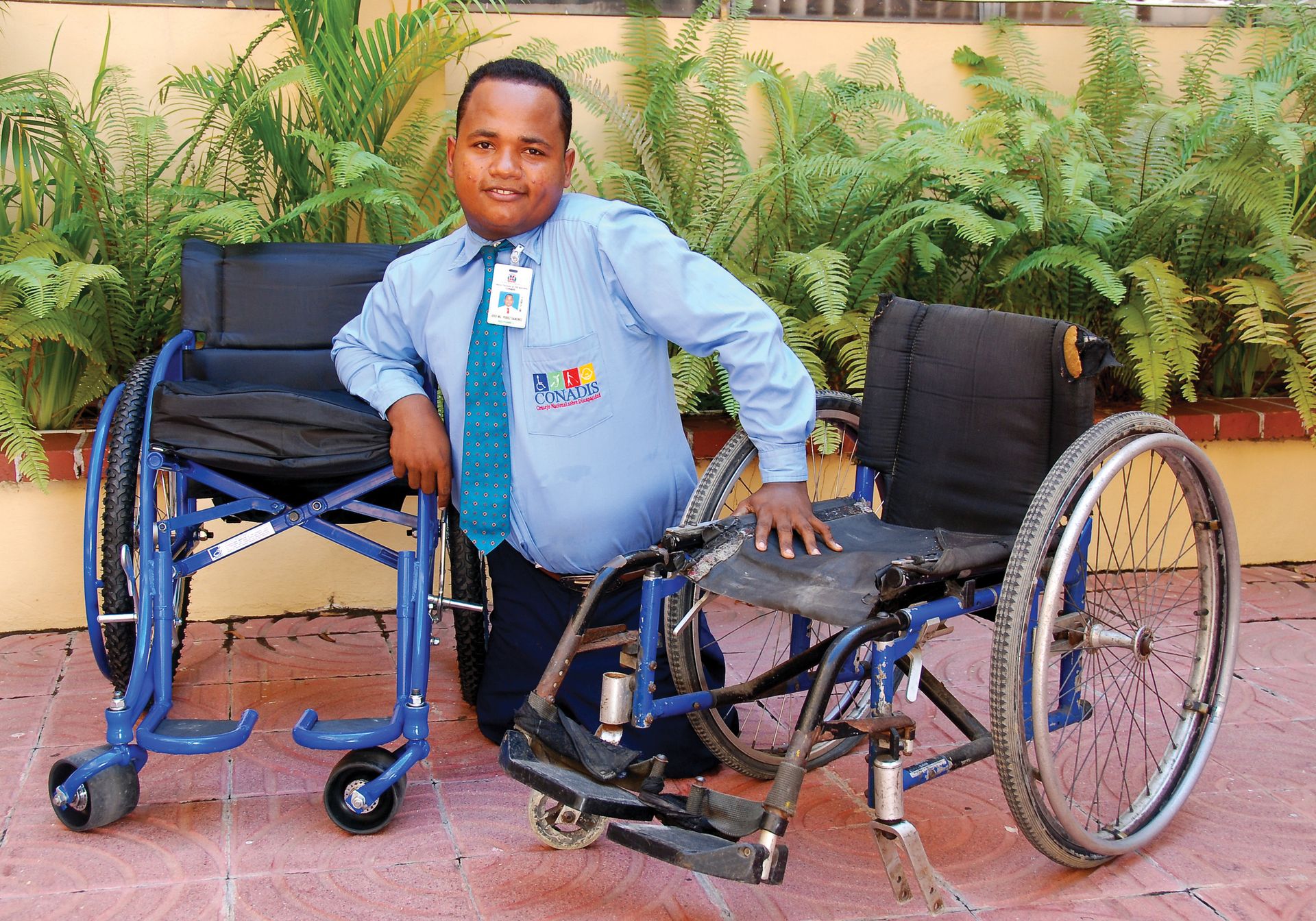 A man in the Dominican Republic balancing himself between an old wheelchair and new one.